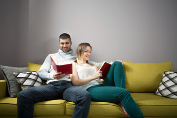 Young woman and man reading a book together. They are sitting on the sofa.