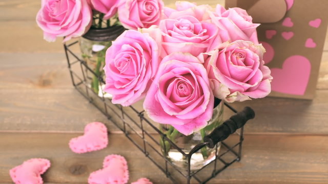 Pink roses in jars on rustic wood table.
