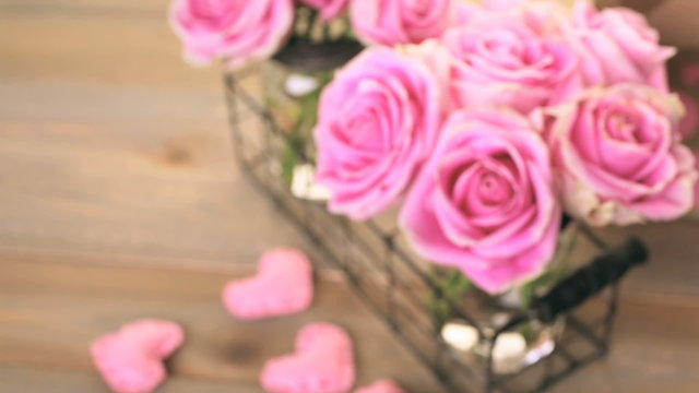 Pink roses in jars on rustic wood table.
