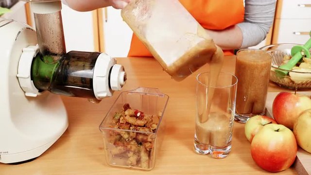 Female hands pouring apple juice in glass. Making drink in juicer machine 4K