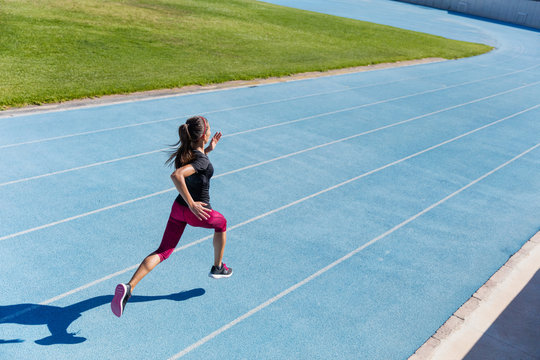 Runner sprinting towards success on run path running athletic track. Goal achievement concept. Female athlete sprinter doing a fast sprint for competition on blue lane at an outdoor field stadium.