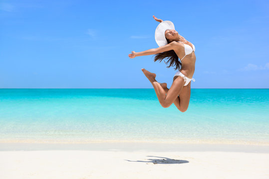 Happy bikini woman jumping of joy on beach. Excited holiday girl doing a jump of freedom and happiness in a free body. Weight loss success healthy lifestyle concept.