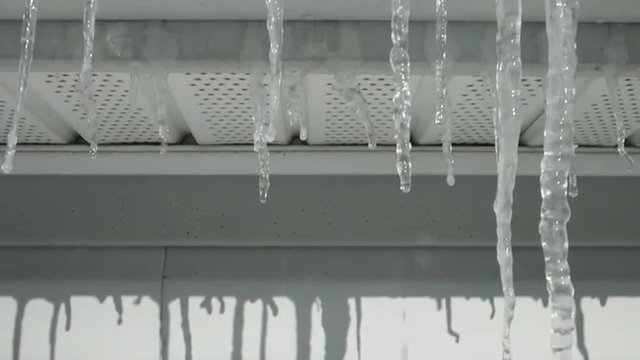Icicles hanging on a house gutter on a sunny winter's day.  Jib move up, across vinyl siding to a close view.  Originally recorded in 4K, UHD.