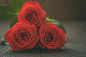 three red roses on wooden table, shallow focus