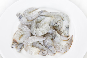 Raw peeled shrimp on white dish on white background.