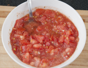 White bowl with tomato, oil, garlic, salt and pepper 