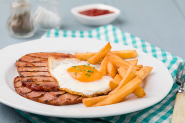 English breakfast with grilled ham, fried egg and french fries.