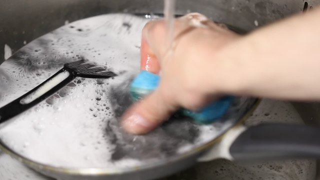 man washes the dishes in the sink with a sponge and detergent