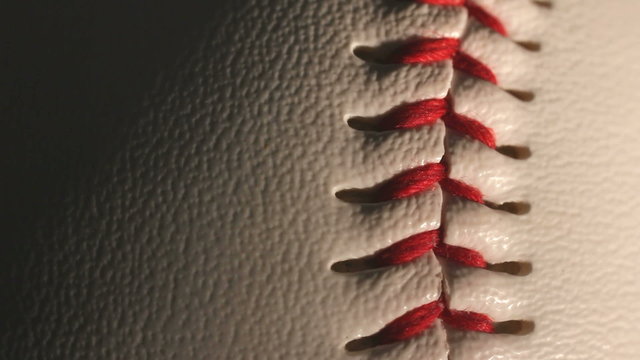 Close up of the red stitching on a rotating white baseball.