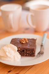 Brownie auf Teller mit Schlagobers und Tassen im Hintergrund