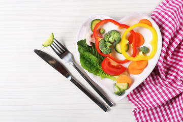 Useful cut vegetables on a plate in the form of heart on wooden table top view