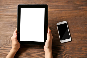 Mobile phone and female hands using tablet, on the wooden background