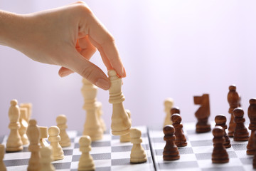 Female hand playing chess on light blurred background