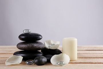 Fototapeta na wymiar Spa stones with white petals and candle on wooden table against grey background