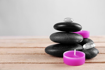 Spa stones with purple candles on wooden table against grey background