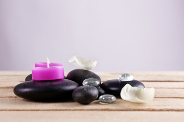 Spa stones purple candles and white petals on wooden table against grey background