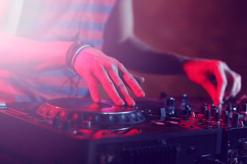 DJ playing music at mixer on colorful blurred background