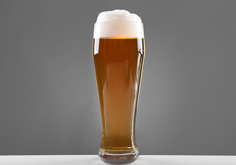 Glass of lager beer with thick froth on grey background