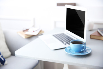 Modern interior. Comfortable workplace. Table with laptop and cup of coffee on it, close up