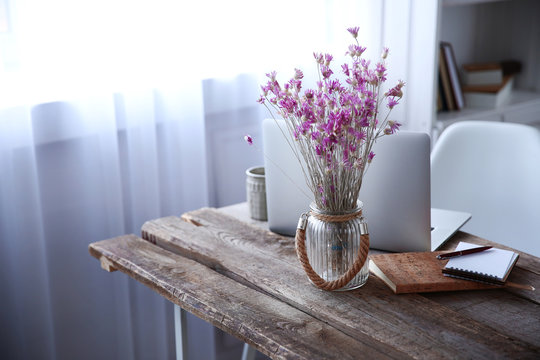 Modern interior. Comfortable workplace. Wooden table with beautiful bouquet of flowers and laptop on it, close up