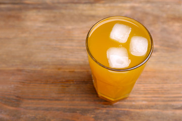 Glass of orange juice with ice block on wooden background
