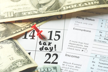 Tax day written and pinned in a calender with dollar bills, close up