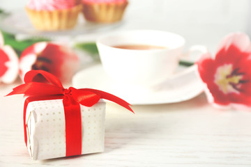 Present box with fresh tulips and cup of tea on wooden table closeup