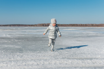 Радостный ребенок бежит по замерзшему озеру в солнечный день ранней весной