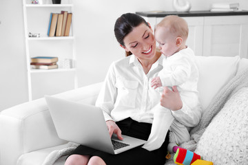 Businesswoman with baby boy on couch working from home using laptop