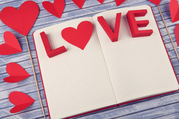 Valentine's Day concept. Beautiful composition of notebook decorated with red hearts on grey wooden background, close up