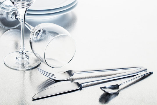 Gl&auml;nzende Gabel, L&ouml;ffel und Messer, Teller und Gl&auml;ser angeordnet auf einer silbernen Edelstahlplatte