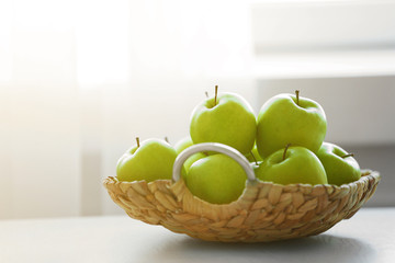 Ripe green apples in a wicker basket on a kitchen table