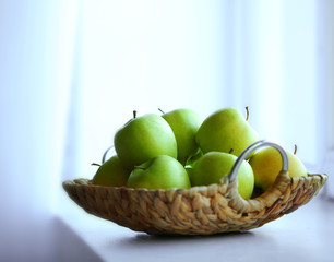 Ripe green apples in a wicker basket on windowsill