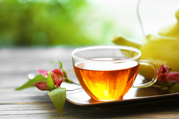 Glass cup of tea with teapot on wooden table against blurred background