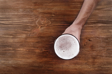 Fototapeta na wymiar Male hand holding glass of beer on wooden background