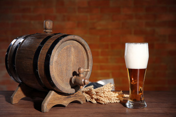 Glass of light beer with wooden barrel and barley ears on brick wall background