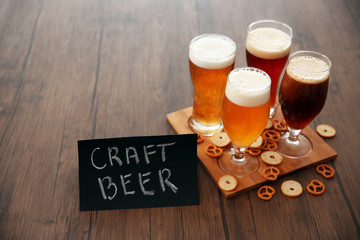Glasses with different sorts of craft beer and snacks on wooden tray