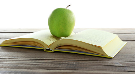 Open book with green apple on table