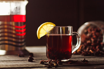 A Cup of hibiscus tea from Sudanese rose with lemon and cinnamon sticks. Brew in teapot on a black wooden background