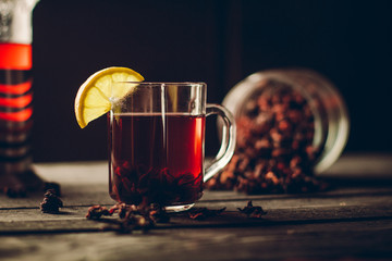 A Cup of hibiscus tea from Sudanese rose with lemon and cinnamon sticks. Brew in teapot on a black wooden background