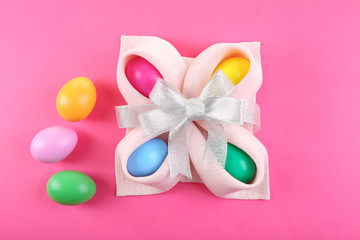 Multicoloured Easter eggs wrapped in napkin with bow on pink background