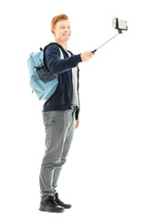 Naklejka premium Young handsome boy with backpack using stick for photo by his self, isolated on white
