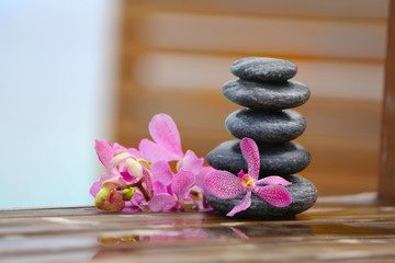 Stack of spa stones with pink orchids on wooden wet bridge
