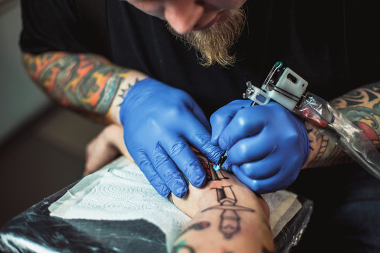 master tattoo artist with a beard makes gloves tattoo on hand men