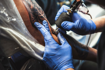 Fototapeta na wymiar master tattooist does the tattoo in gloves on the hand of the man