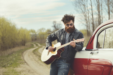 Bearded man playing guitar outdoors near retro car