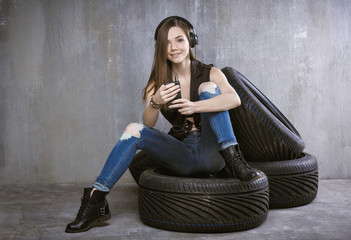 young girl with headphones and mobile phone, sitting on car tire
