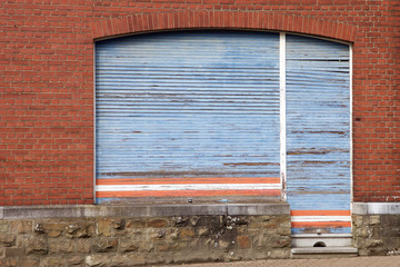 Geschlossener blauer Rollladen eines alten Ladenlokals mit horizontalen roten und weißen Streifen