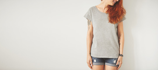 Young girl wearing grey blank t-shirt and blue jeans shorts. Concrete wall background with copy...