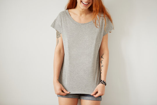 Girl wearing grey blank t-shirt standing on the background of a white wall.